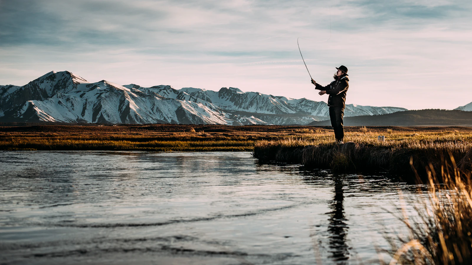 Angler casting from the bank of a still mountain lake at dusk